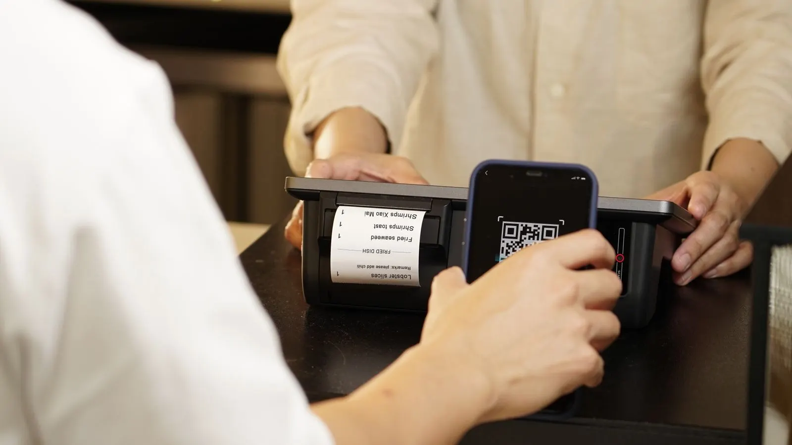 A customer at a counter scanning a QR code with their phone while paying