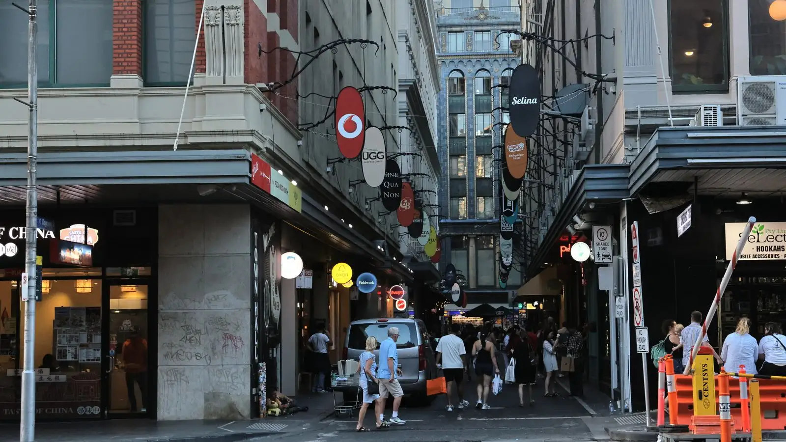 A busy Melbourne laneway lined with shopfronts, cafe signs and people walking through